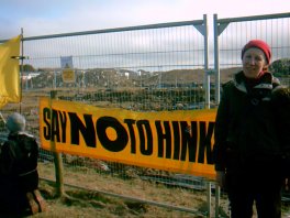 Jill standing next to 'No to Hinkley' banner on fence with mud visible beyond