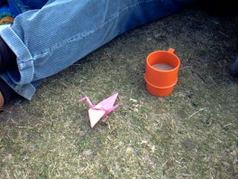 Pink paper crane on grass next to coffee-cup