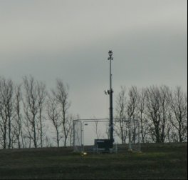 Tall pole with camera in fenced enclosure on horizon