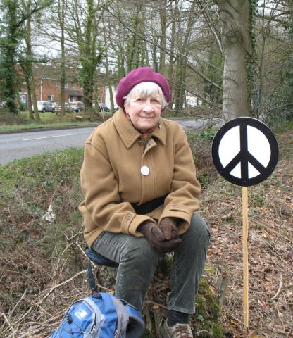 Barbara Bampton with placard, sitting on a tree stump